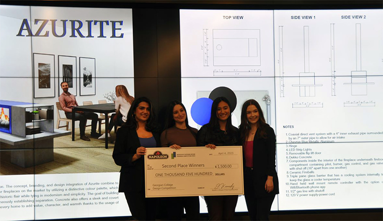 Four females stanging on a stage in front of a video screen. They're holding up a large cheque.
