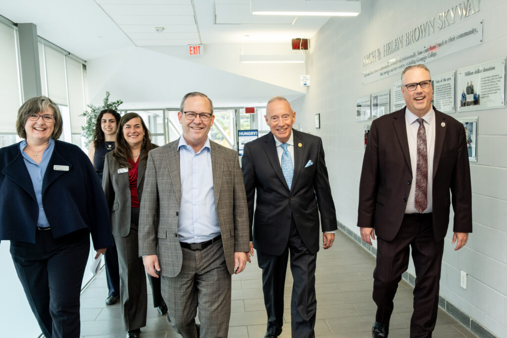 A group of people walk down a hallway and all smile at the camera.