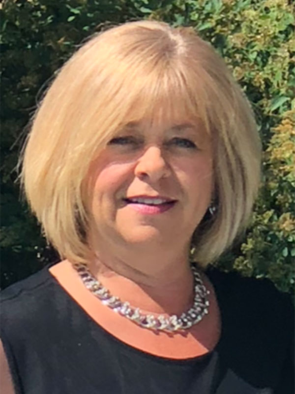 Person with short, blonde hair and bands wearing a silver necklace and black shirt smiling