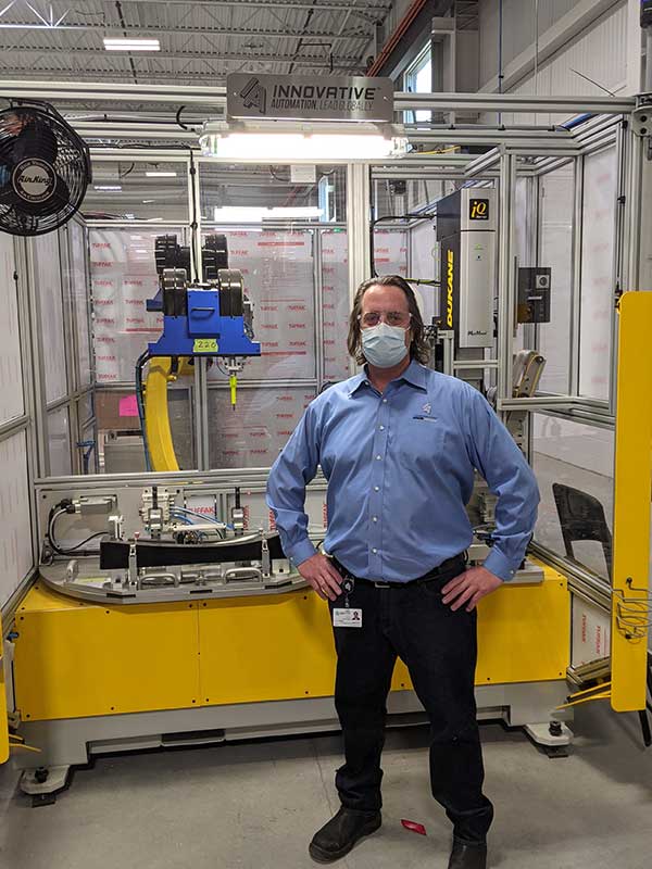 Person in a blue dress shirt, dark jeans, work boots and a mask standing in a factory