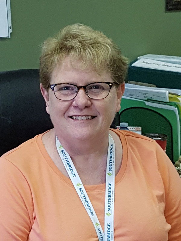 Person with short, blonde hair and glasses wearing an orange shirt and white branded lanyard smiling