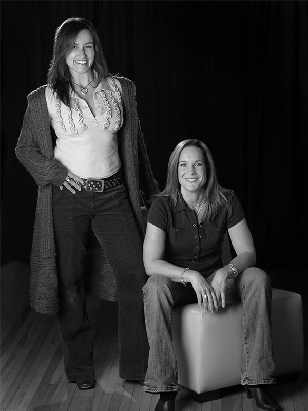 Black and white photograph of two people, one standing and one sitting on an ottoman