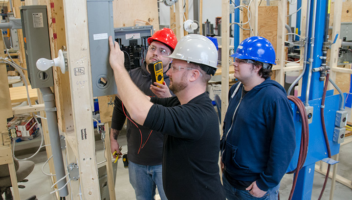 A group of Electrical Techniques students wearing hard hats and using a multimeter tool to check the voltage on a control panel