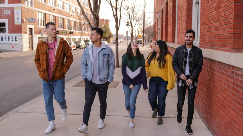 5 teenage students, 2 females and 3 males walking down a street