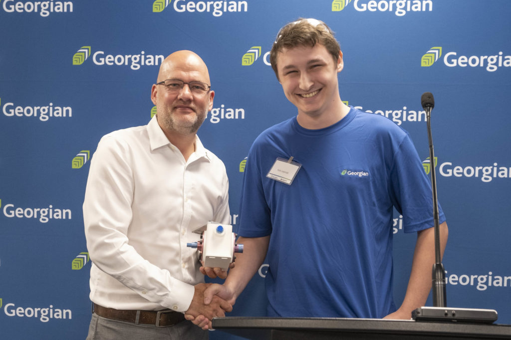 an older white male with glasses shaking hands with a young white male.