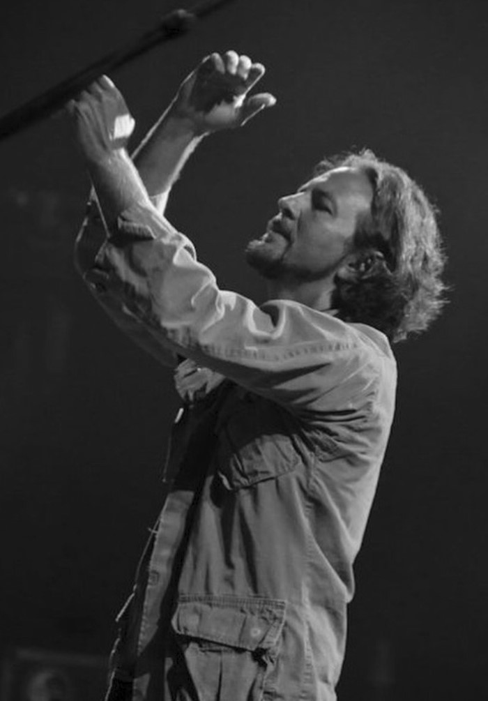 A black-and-white image of a person singing on stage at a concert. 