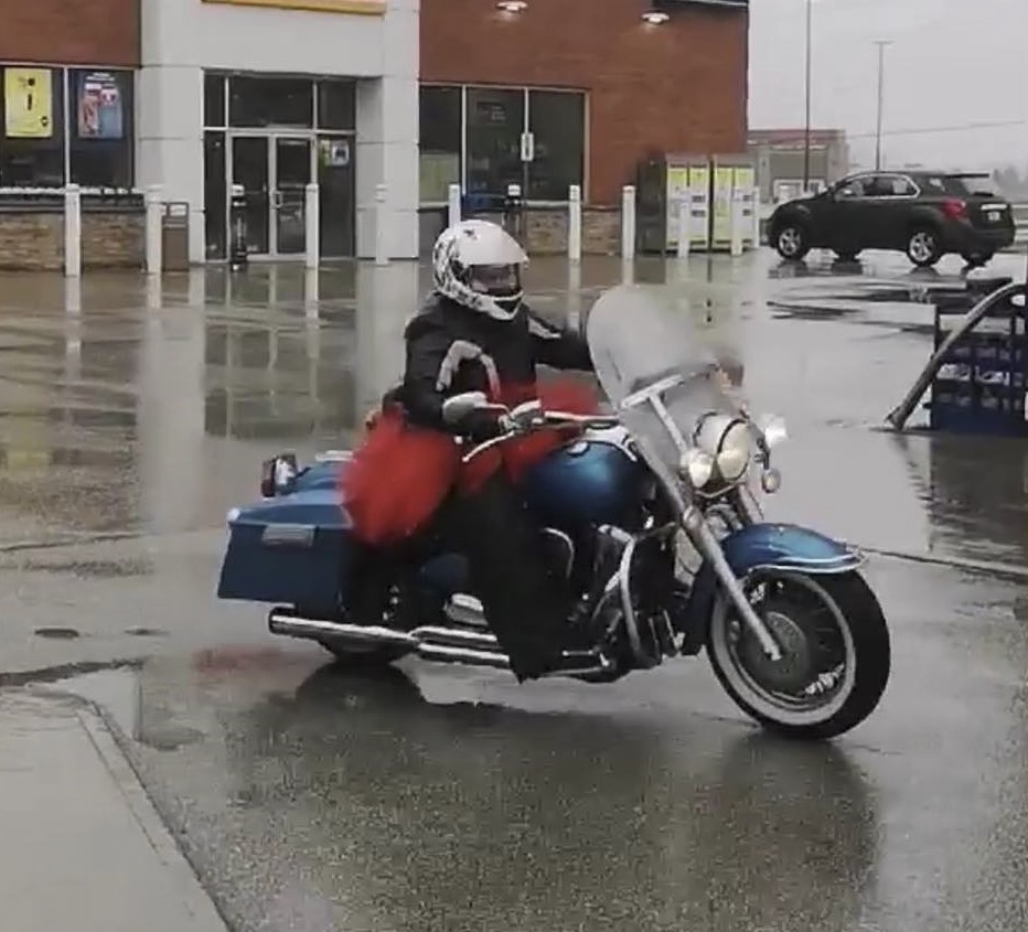 A person rides a blue motorcycle through a parking lot. 