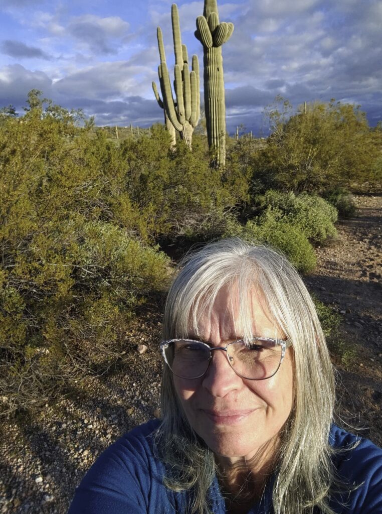 A person takes a selfie while standing near cacti and shrubbery.
