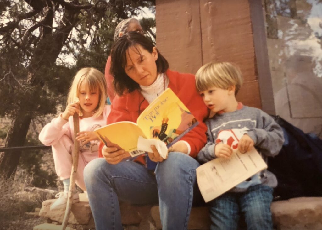 An adult and two children sit outside and read a book together.