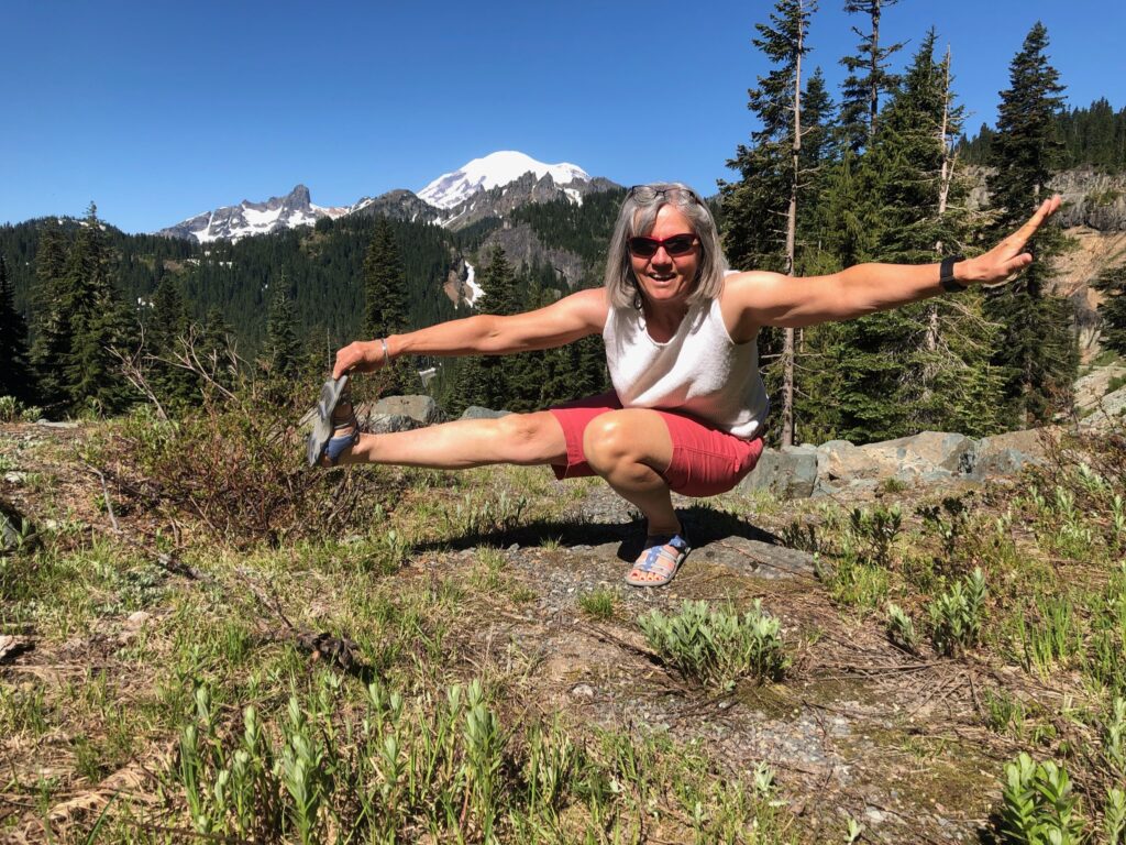 A person does a pistol squat on a hill with a mountain range in the background.