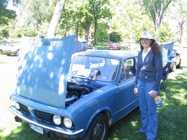 A person stands next to a vintage car with its hood up.