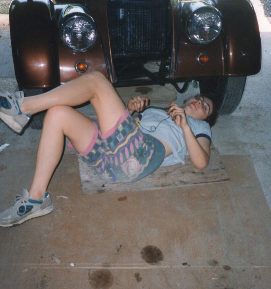 A person lies on the ground under a car.