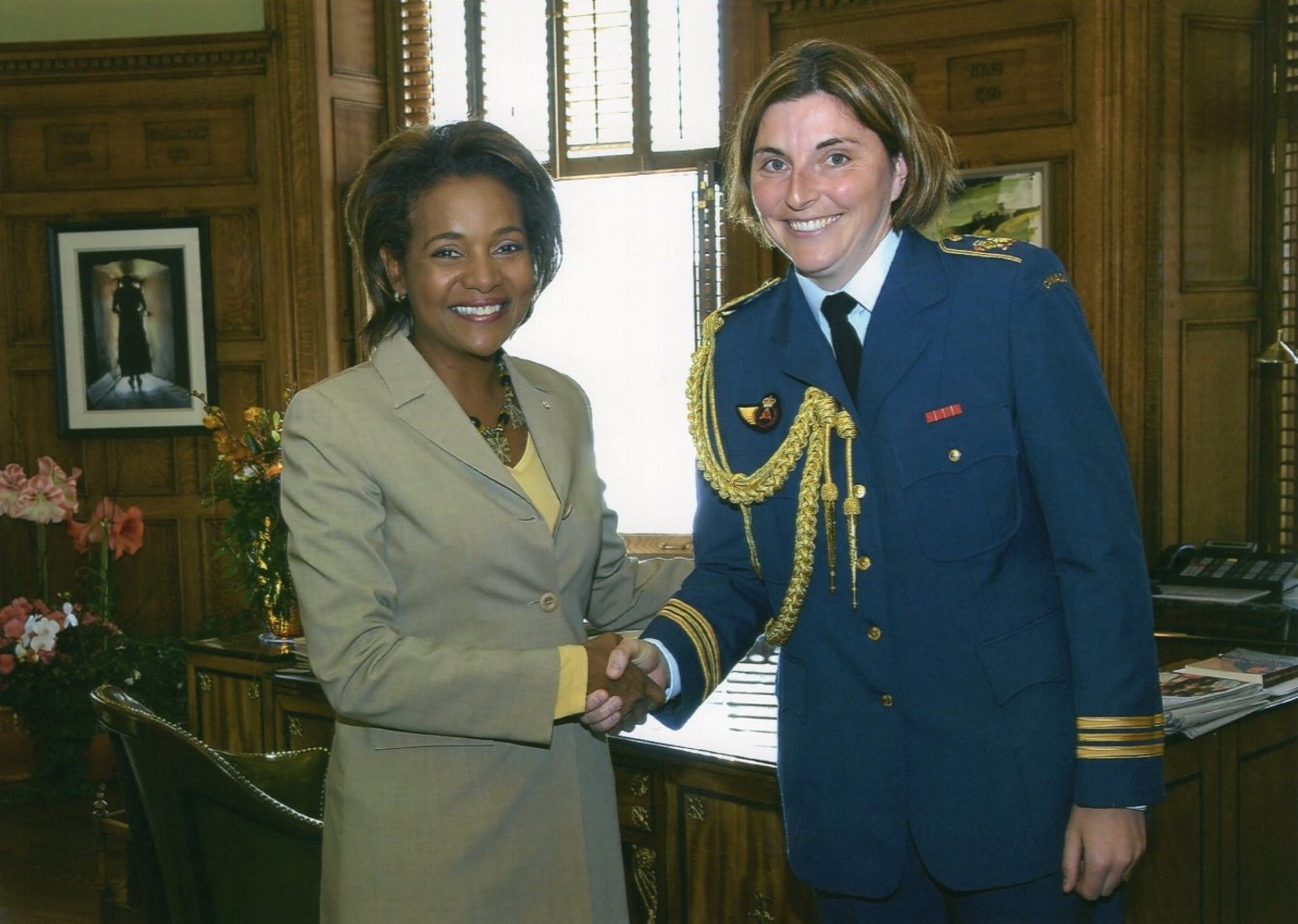 Two people, one of whom is wearing a military uniform, shake hands in an office.