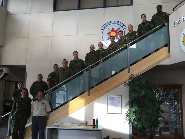 Fourteen people wearing military uniforms stand on steps leading up a staircase.