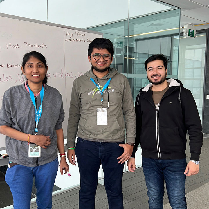 Two young males and one female smiling and standing in front of a glass wall.