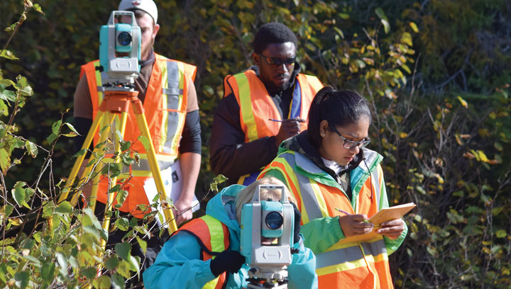 Four environmental surveyors wearing reflective safety vests using tacheometer equipment and taking notes
