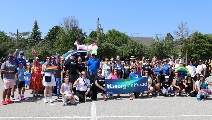 A group of people in Georgian-branded and Pride-themed clothing gathered together with a #GeorgianProud banner at the Barrie Pride Parade on June 3, 2023