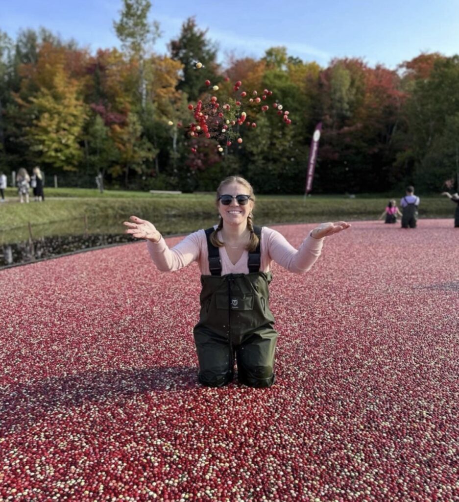 A person wearing waders stands in the middle of a pool of cranberries and throws some up into the air.