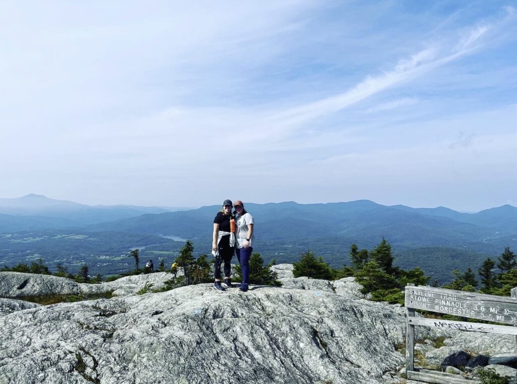 Two people stand at the top of a rocky hill overlooking a sprawling landscape. 