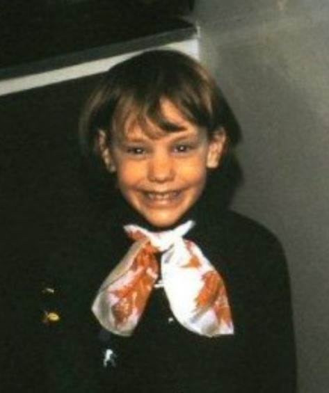 A child wearing a Brownies uniform of brown dress and white and red scarf.