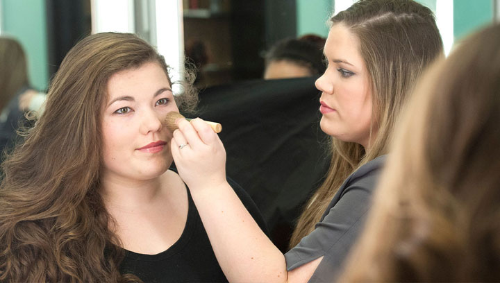 Esthetician student using a brush to apply foundation to a client's cheek in a salon setting