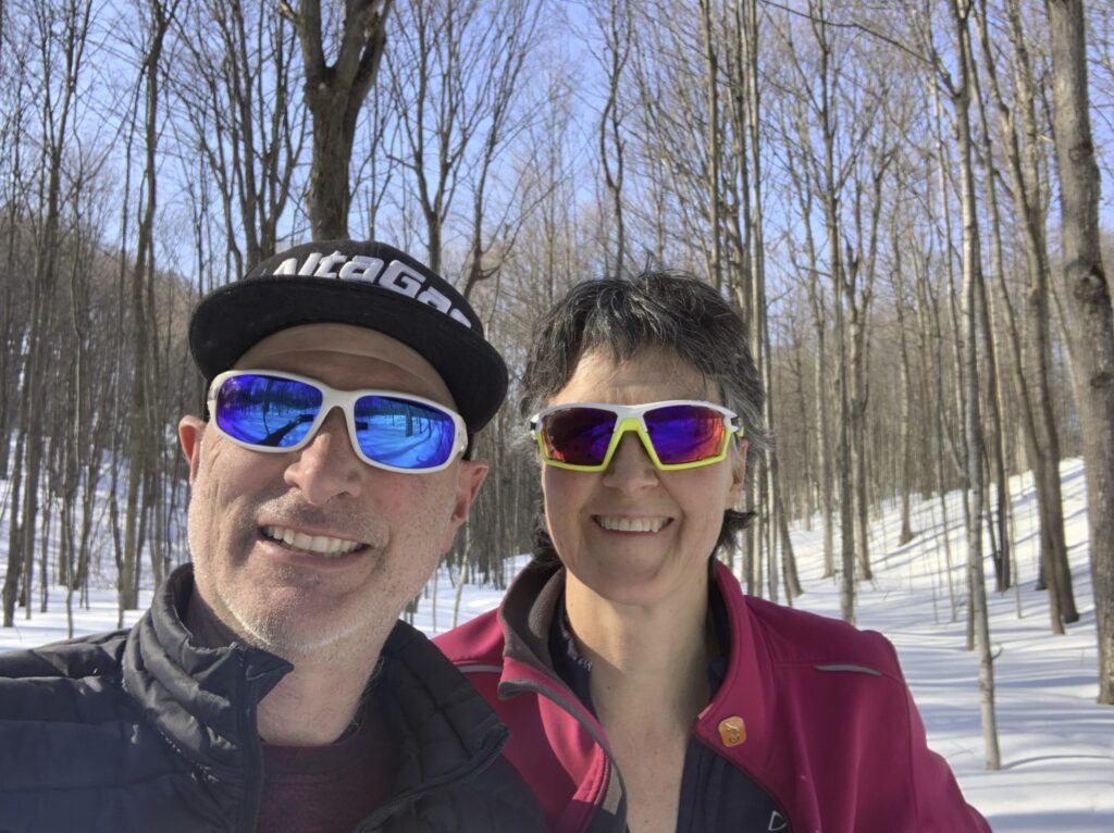 Two people standing outside in a snowy forest take a selfie. 