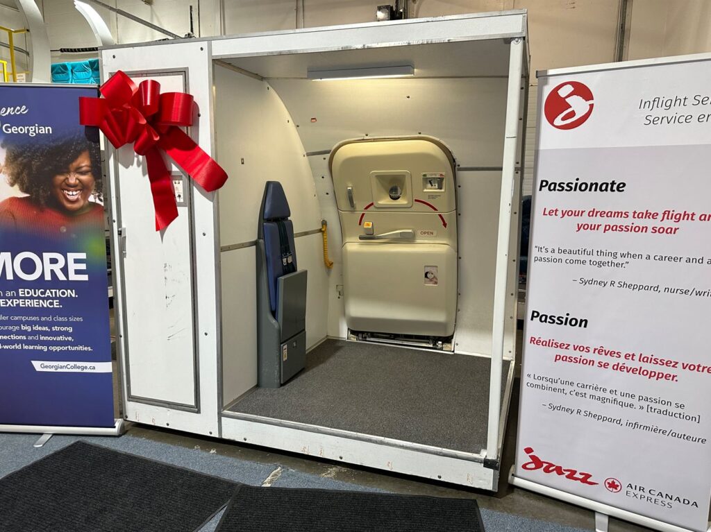 A Boeing 757 door training, which includes the plane door and entrance, with an oversized red bow on it.