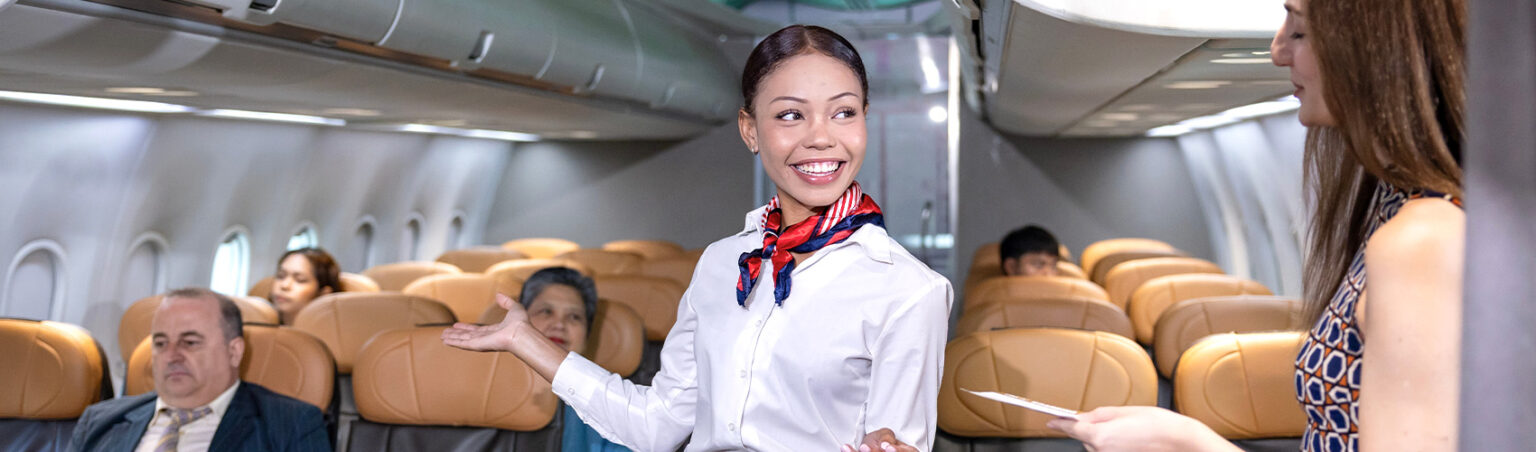 A flight attendant in uniform on a airplane checking checking in a passenger