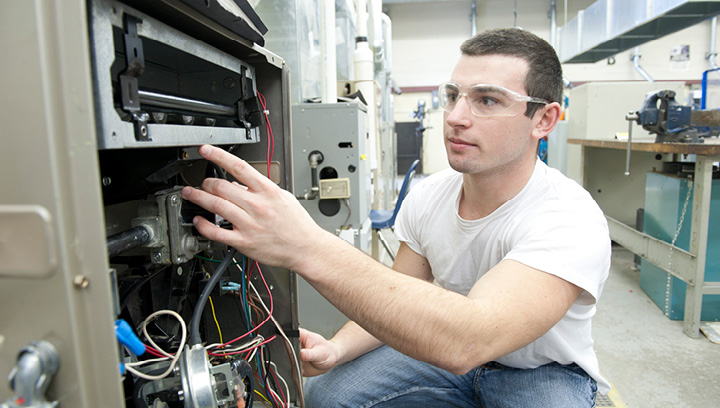 A Gas Technician student wearing jeans, a white t-shirt and safety glasses repairing a piece of equipment in a lab