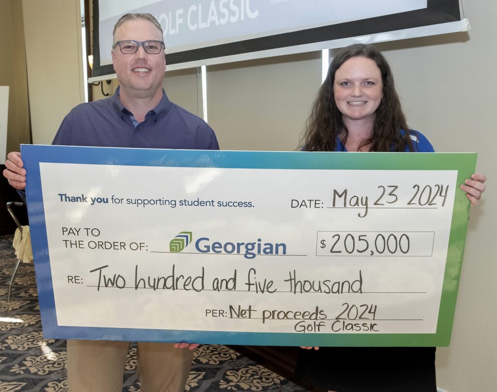 Two people stand together and hold an oversized cheque to СŶƵ for $205,000 from the 2024 Golf Classic.