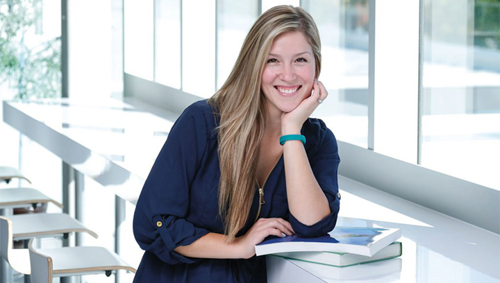 female student leaning on two textbooks on a counter table while smiling