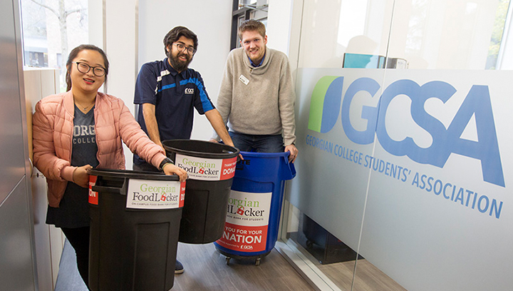 Three people in the GCSA office holding СŶƵ FoodLocker donation bins