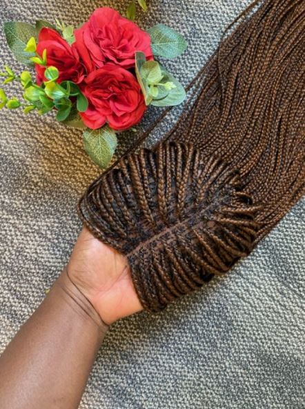 An aerial view of a hand holding a brown, braided wig.