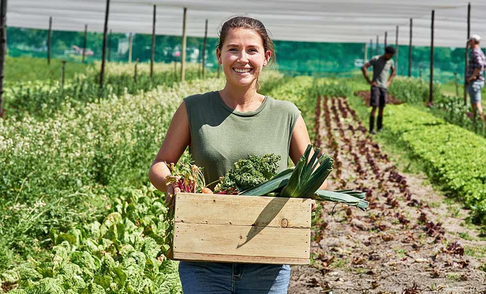 A woman holding a box of vegetables.