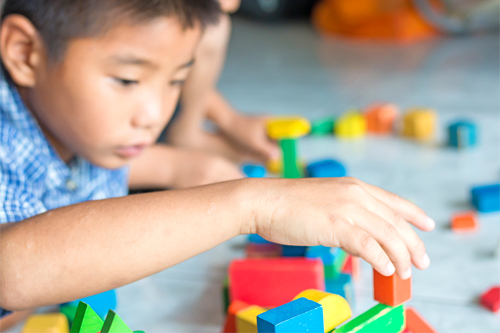 young child's hand stacking colourful, wooden block toys