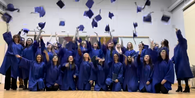 A group shot of people dressed in blue graduation gowns throwing their grad hats up in the air