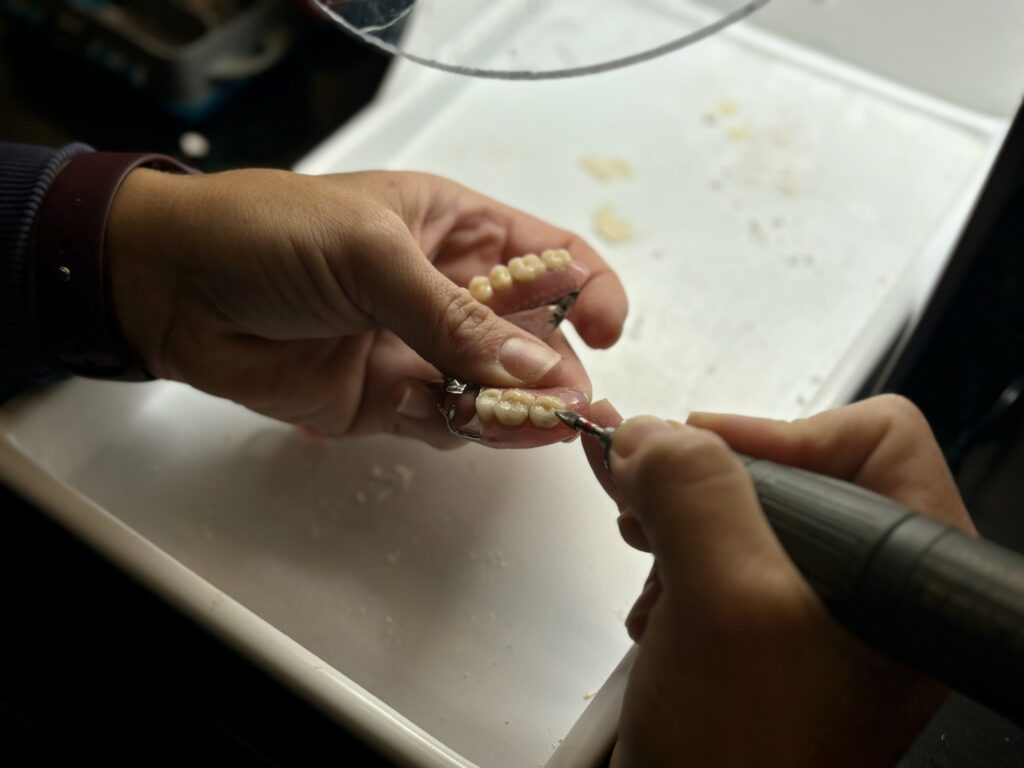 A closeup of a pair of hands and tool working on a pair of dentures in a workshop.