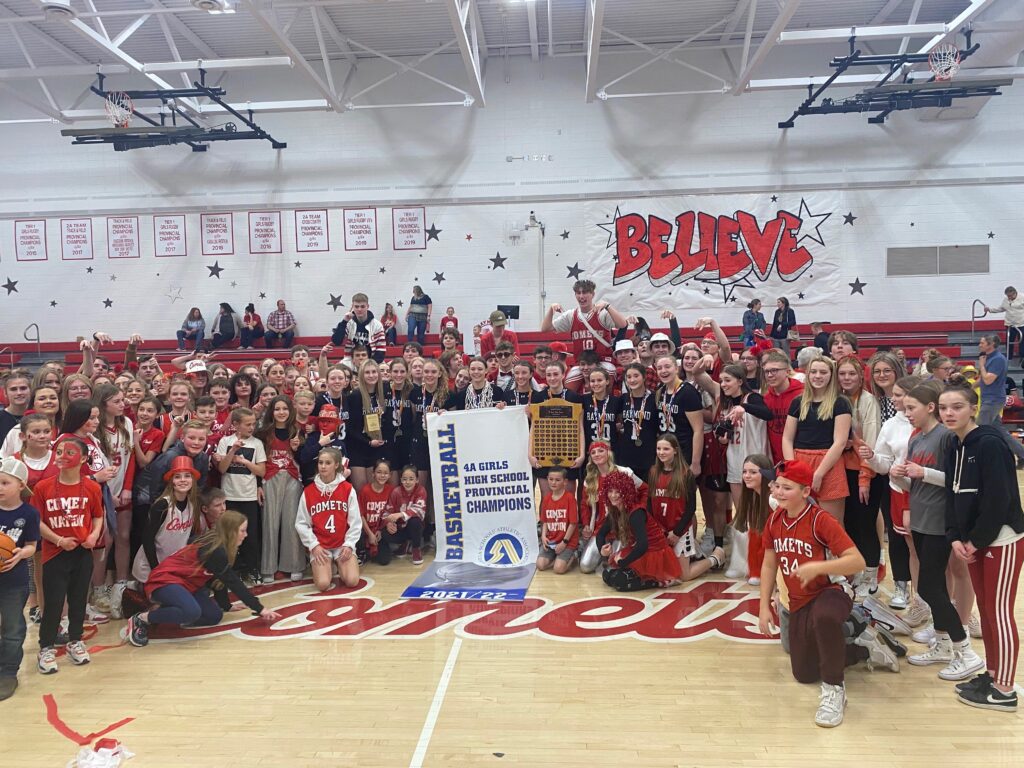 A group photo in a gym of a high school basketball team and other students at the school all dressed in red and white.