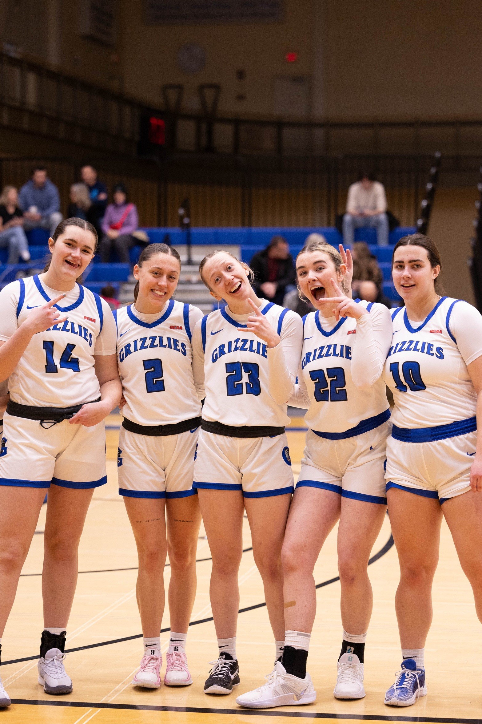 Five people wearing basketball uniforms reading "Grizzlies" make silly poses while standing together on a basketball court.