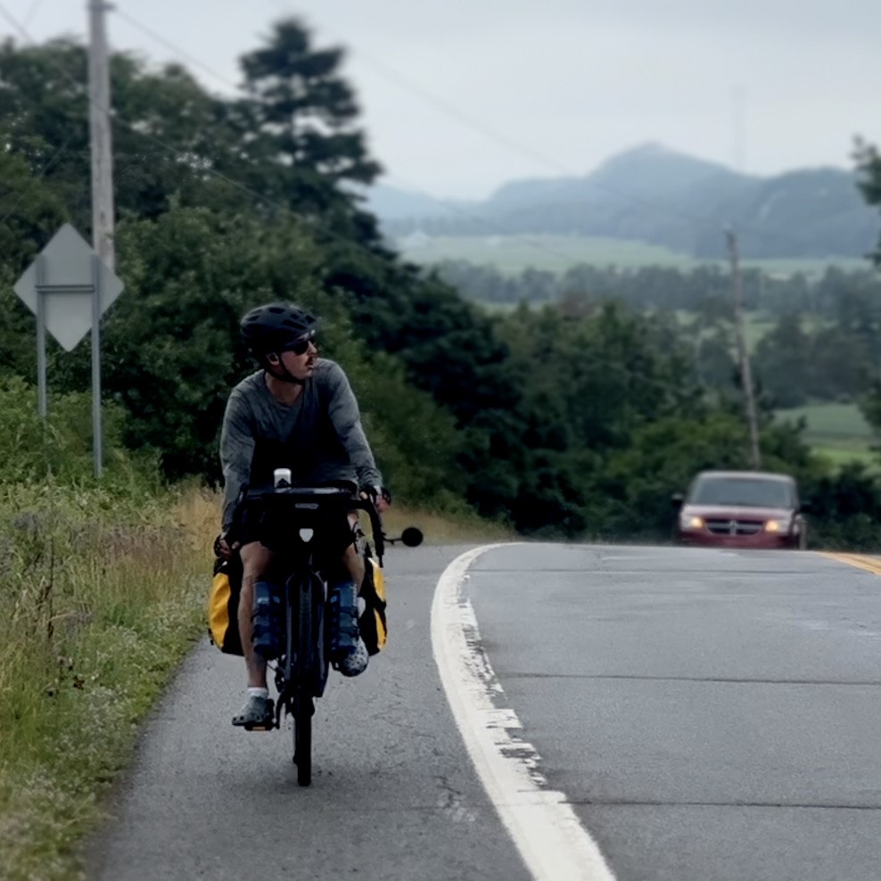 A person rides a bike down a road through a landscape of hills and woods. 