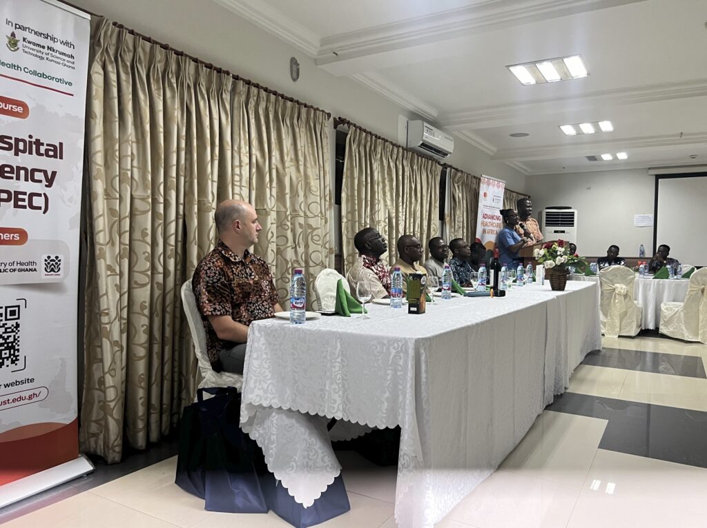 Several people sit at a long table at the front of a room during a banquet. 