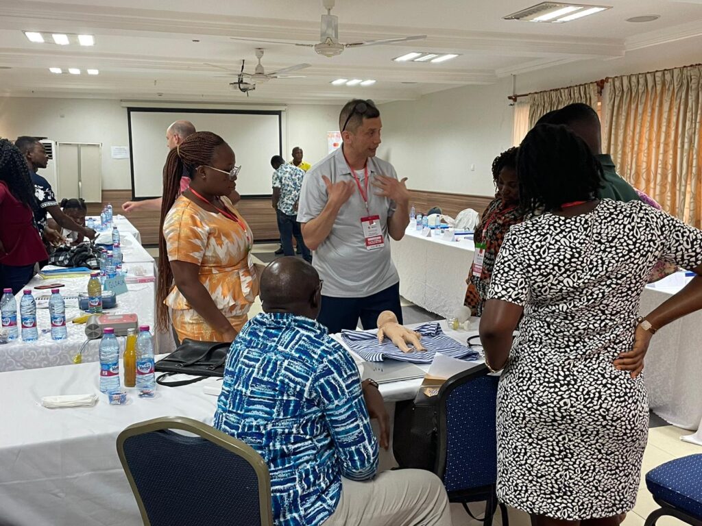 A person gestures with their hands while speaking to a few people standing around a table. 