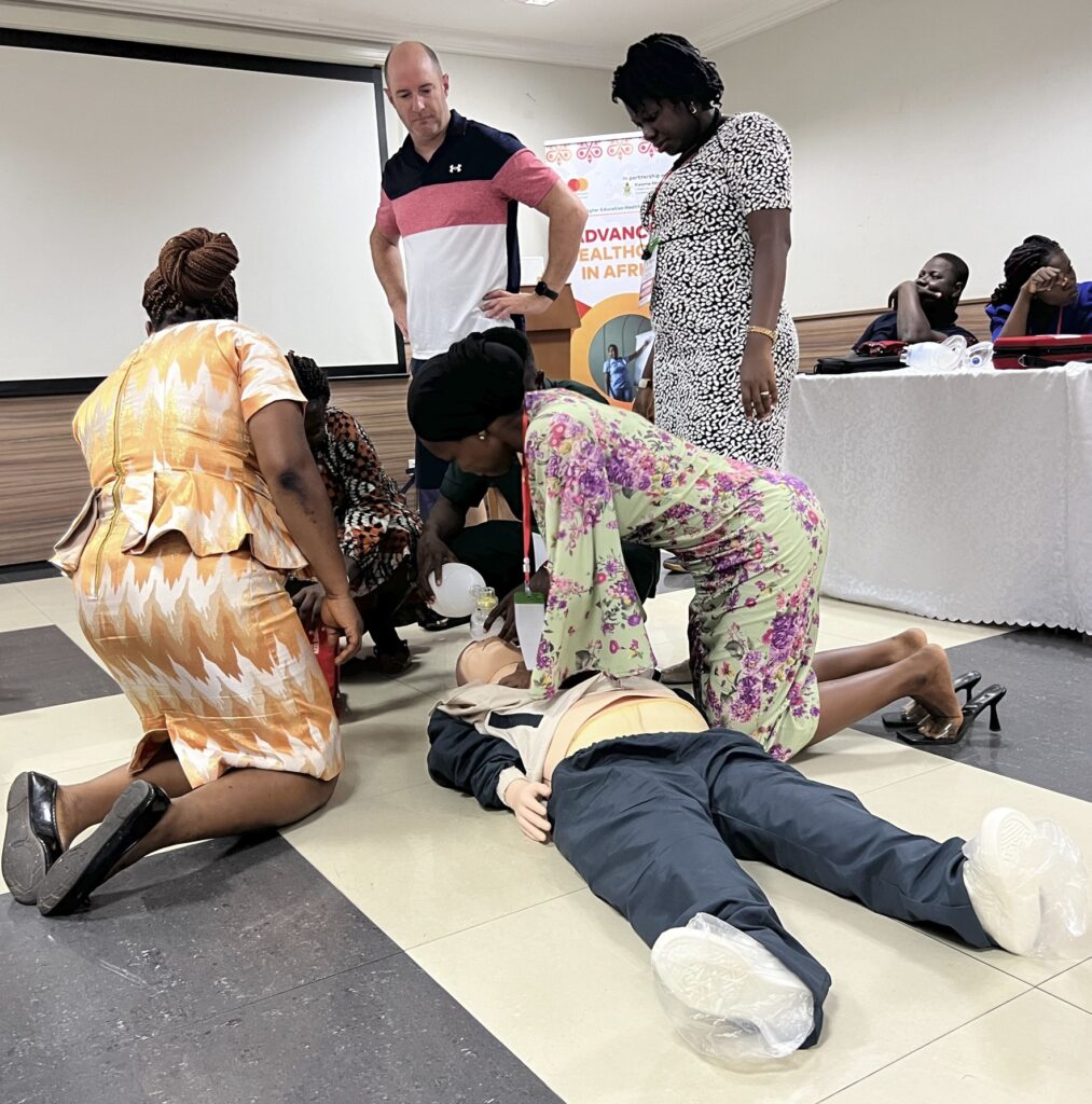 Two people stand next to a few people kneeling next to a simulator patient for which they're providing medical care.