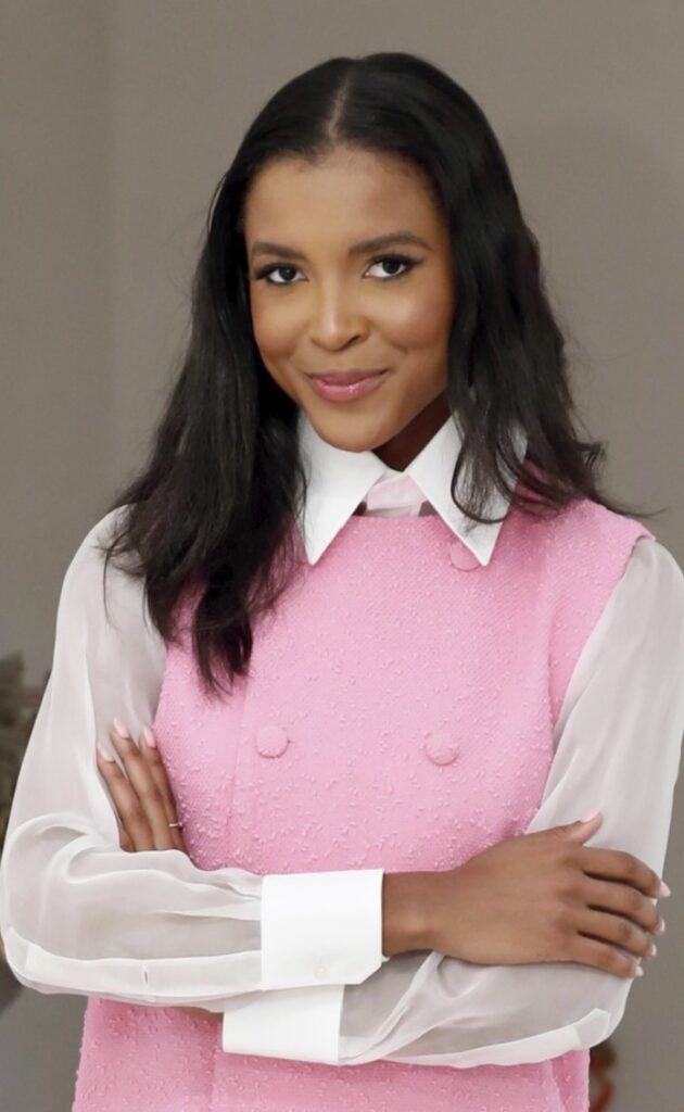Headshot of a person with long black hair and who's wearing a white collared shirt and pink vest. 