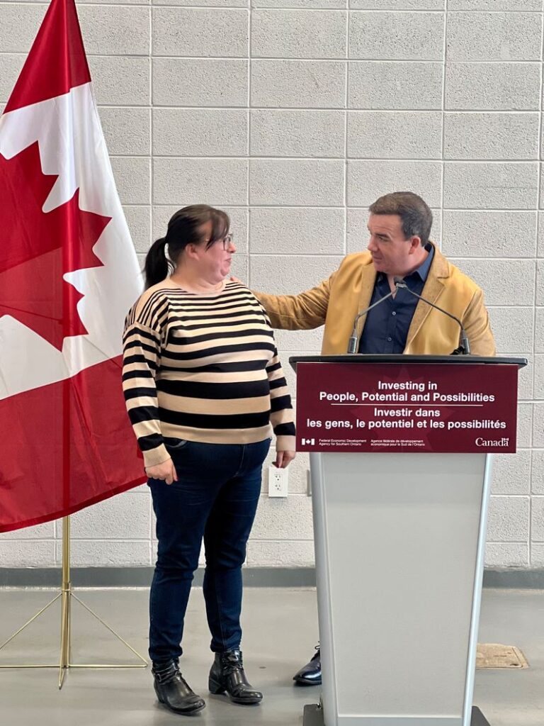 Two people stand at a podium next to a Canada flag.
