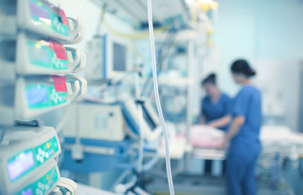 Registered Nurses in blue scrubs standing next to a patient on a bed in a hospital room
