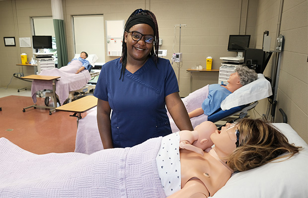 BScN student Zawadi Mukwege standing next to human patient simulators in the Owen Sound nursing lab