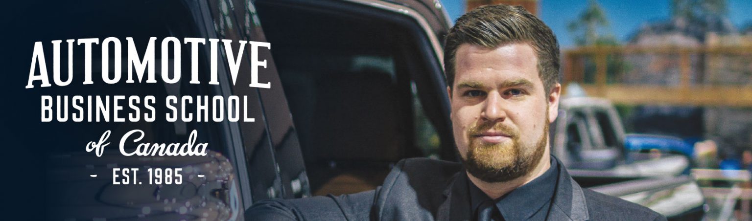 Automotive student with slicked back hair and a beard wearing a black suit and tie while leaning against a black Dodge Ram truck