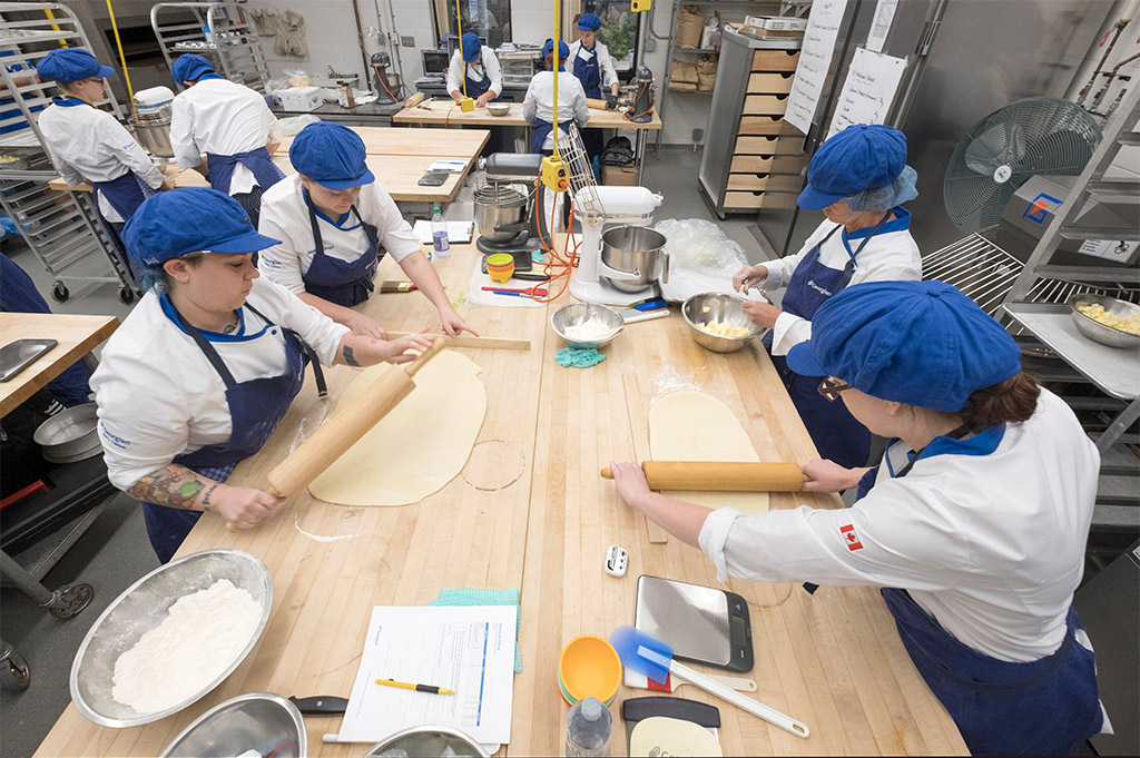 Georgian College Baking and Pastry arts students wearing uniforms, aprons, hair nets and hats making pastry in the baking lab