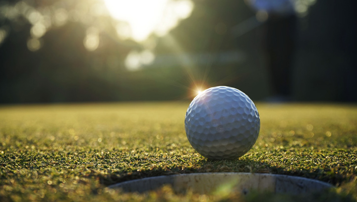 A white golf ball next to a hole on the golf course during a sunny day